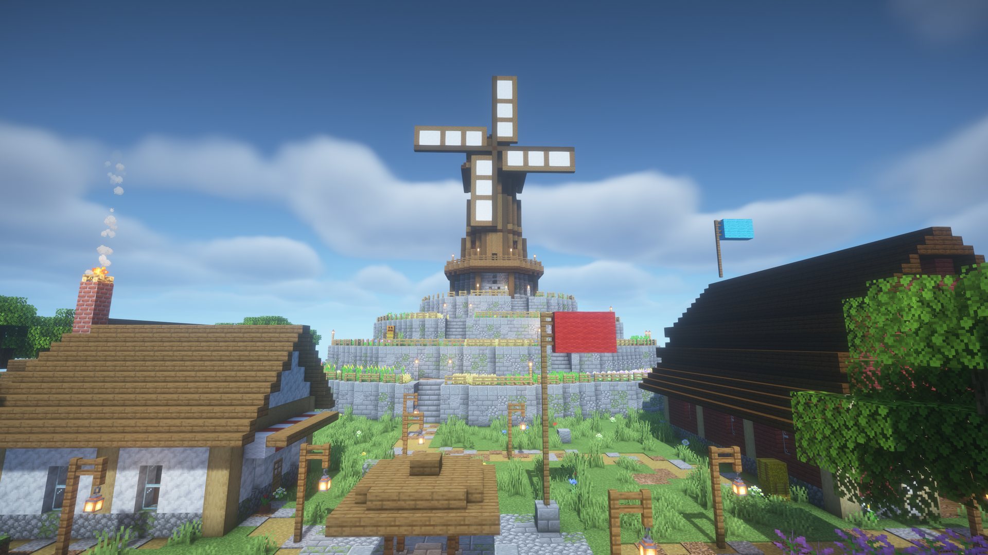 A windmill on a terraced hill above a village plaza with a well, a cottage and a red barn